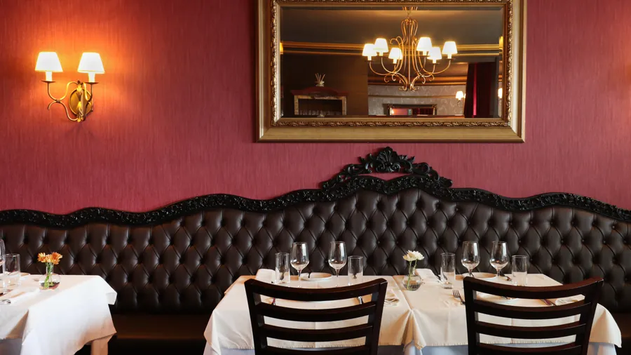 Banqueta capitonê marrom sob espelho de moldura dourada na parede bordeaux